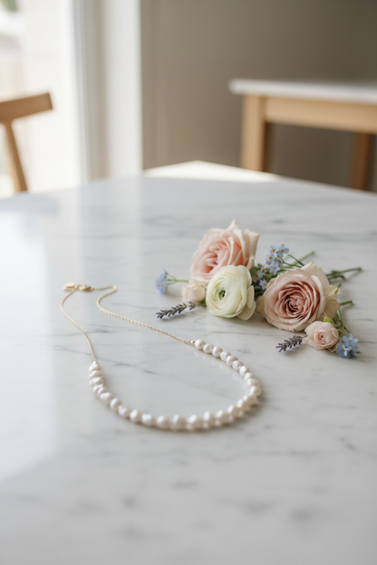 Pearl necklace draped on marble with pastel flowers